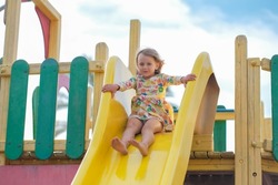 Child playing on outdoor wooden playground. Kids play on school or kindergarten yard. Active kid on colorful slide. Healthy summer activity for children
