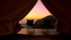 Tourist tent in camp among with mountain view on sunrise. View from tent camping on amazing sunrise with mountains and two folding camping chair. Travel vacation on nature