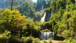 Beautiful waterfall in green tropical forest. Mountain jungle with limestone waterfalls cascades. Famous largest, highest waterfall in Thailand. Powerful raging whitewater falling stream. Slow motion.