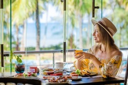 Tropical vacation. Breakfast in modern hotel resort with sea and palm trees on background. Traveler woman on summer holidays on Phuket, Thailand. Exotic travel in Southeast Asia
