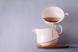 a cup of tea balances on a white ceramic teapot, copy space