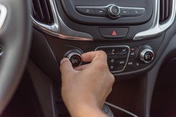 Left hand turning knob on modern car cooling temp adjust to 64 Fahrenheit (F) degree. Asian male hand on dashboard air conditioner car interior