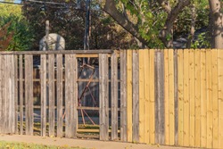 Close-up new wooden fence near collapsed aged slats in backyard of residential house with tall tree in suburban Dallas, Texas, America. New privacy wall installation boards lumbers of corner house