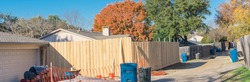 Panorama view new fence installation with orange safety net at residential house near Dallas, Texas, America. Lumber board garden fence with colorful fall foliage at suburban back alley