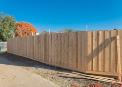 Close-up new fence installation at residential house near Dallas, Texas, America. Lumber board garden fence with colorful fall foliage at suburban back alley