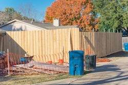 New fence installation with orange safety net at residential house near Dallas, Texas, America. Lumber board garden fence with colorful fall foliage at suburban back alley