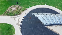 Aerial view kids playing in water fountain, reflecting pool at Doris Miller Memorial in Waco, TX, metal panel installation representing of USS West Virginia in WWII, sculpture. Black Pearl Harbor hero