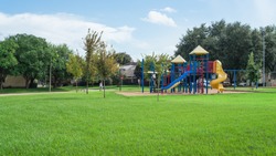 Colorful children playground activities in public park surrounded by green trees in Houston, Texas. Children run, slide, swing on modern playground. Urban neighborhood childhood concept. Panorama.