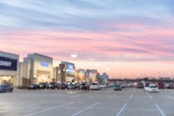 Blurred image exterior view of empty parking lots in modern shopping center in Humble, Texas, US at sunset. Mall complex outdoor uncovered parking and bokeh light of retail store in background.