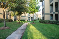 Clean lawn and tidy oak trees along the walk path through the typical apartment complex building in suburban area at Humble, Texas, US. Grassy backyard, sunset warm light.