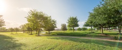 Panorama view of urban park near residential area neighborhood in Sugarland, Texas, US. Beautiful green grass lawn, oak trees and walking/biking path illuminate by sunshine during early spring morning