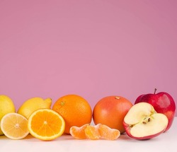 Composition with fresh sliced peeed fruits apple, grapefruit, orange, lemon, apple, avocado on a table isolated on a pink background