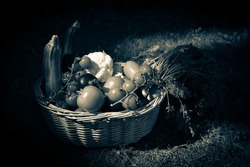 Still life vintage style photography of a wicker basket full of vegetables. Monotone dark background. 