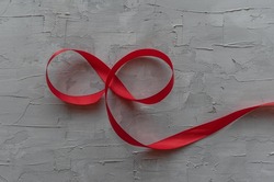 On a gray background, a red ribbon in the form of an eight or infinity.