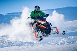 Snowmobile riding with fun in deep snow powder during backcountry tour. Extreme sport adventure, outdoor activity during winter holiday on ski mountain resort