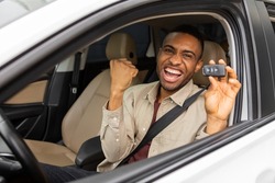 Joyful african american guy holding auto key shaking fists sitting in automobile 