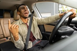 Joyful black man dancing in car, singing while driving his car. Road fun