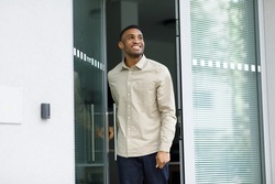 A cheerful black man leaves the house, opening the glass door.