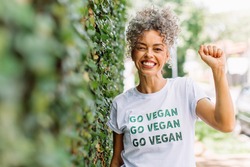 Vegan activist smiling cheerfully while standing alone outdoors. Happy mature woman advocating for veganism while wearing a shirt with the words 