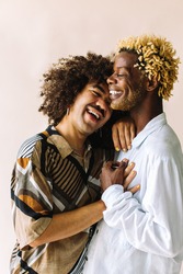 Carefree young gay couple standing together in a studio. Two affectionate male lovers smiling cheerfully while embracing each other against a studio background. Young gay coupe being romantic.