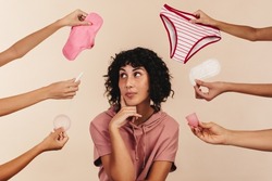 Young woman contemplating the best sanitary choice for her body. Thoughtful young woman looking away while surrounded by hands holding different reusable and non-reusable sanitary products.