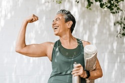 Happy elderly woman celebrating her fitness achievement after a great outdoor workout session, flaunting her strong bicep. Fit senior woman expressing her pride in her successful exercise routine.