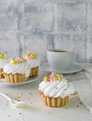 Fresher cake basket with sprinkles and cream of whipped cream on a light table. Coffee in a white cup and a light napkin in the background. Brick background, dessert spoon on the table