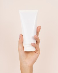 Hand holding Cosmetic plastic tube isolated on beige background.