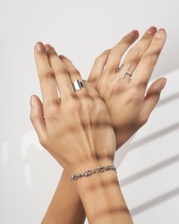 Hand wearing silvers jewelry bracelet and rings on soft white background. Still life and creative photo with shadows.