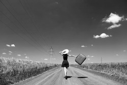 Lonely girl with suitcase at country road. Photo in black and white color style.