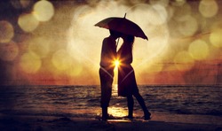 Couple kissing under umbrella at the beach in sunset. Photo in old image style.