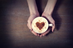 woman holding hot cup of coffee, with heart shape