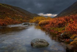 Stormy sky and fog in mountains. Red and yellow autumn northern meadow. Autumn in tundra. Lapland.