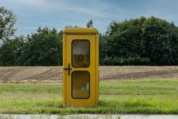 old yellow phone booth on a meadow outside the city
