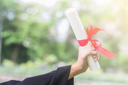Happy graduate young Asian woman wear black gown and holding a certificated in hand with garden background, Education concept