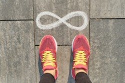 Infinity sign on gray sidewalk with woman legs in sneakers, top view.