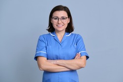 Portrait of confident smiling female nurse with arms crossed looking at camera, over gray background