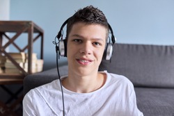Portrait of student boy teenager in headphones looking at webcam, video lesson, videocall, online training. Gray inside background
