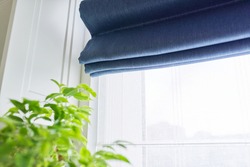Roman blind in the interior detail close-up. Curtain blue blackout fabric, sheers white linen, fashionable modern window decoration design at home