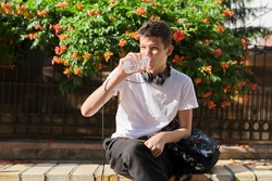 Teenager guy drinking water from bottle and removing thirst on hot summer day in the city
