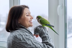 Middle aged woman and parrot together, female bird owner talking looking at green quaker pet