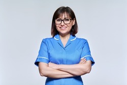 Portrait of middle aged nurse in blue uniform looking at camera on light studio background