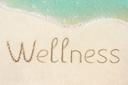 Wellness concept photo. Word Wellness handwritten on the sand. Beach and soft wave background.