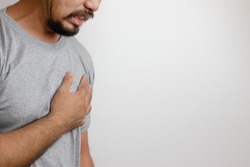 A man in a gray T-shirt holds his hand to his chest as sudden chest pain is an unhealthy sign leading to heart disease. Aortic stenosis and other ailments. White background. Empty space for text.