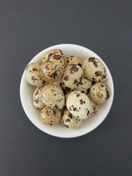 Small har boiled quail eggs in the white ceramic bowl. Black background. Locally known as telur puyuh. Speckled brown on the surface. Avian eggs. Malaysia.