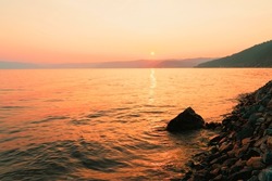 Picturesque sunset in golden orange colors on rocky beach and sea late summer evening