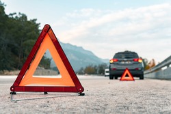 The warning triangle is at the back of the car at a safe distance.Car on the road behind warning triangle.The triangle placed behind the car.
