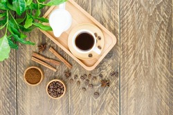 a cup of aromatic coffee and a milkman with milk on a tray. morning breakfast .green arabica coffee leaves on a wooden background