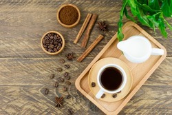 top view of a wooden tray with a cup of hot coffee and a milkman with milk to improve the taste. brown wooden table with Arabica coffee leaves