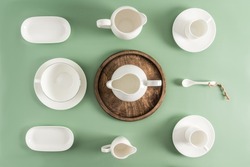 white ceramic and porcelain cups, saucers, milk jug of different shapes on a light green background. top view. flat lay